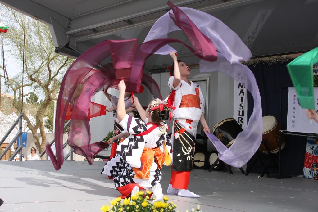 Japanese woman dancers, in traditional costume, swirl colorful sheer cloths around them in fluid motion.